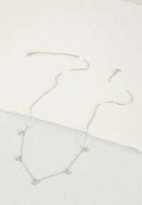 Collier en chaîne argentée avec cinq accents décoratifs, maillons délicats et fermoir sécurisé, reposant sur une surface légère et texturée.