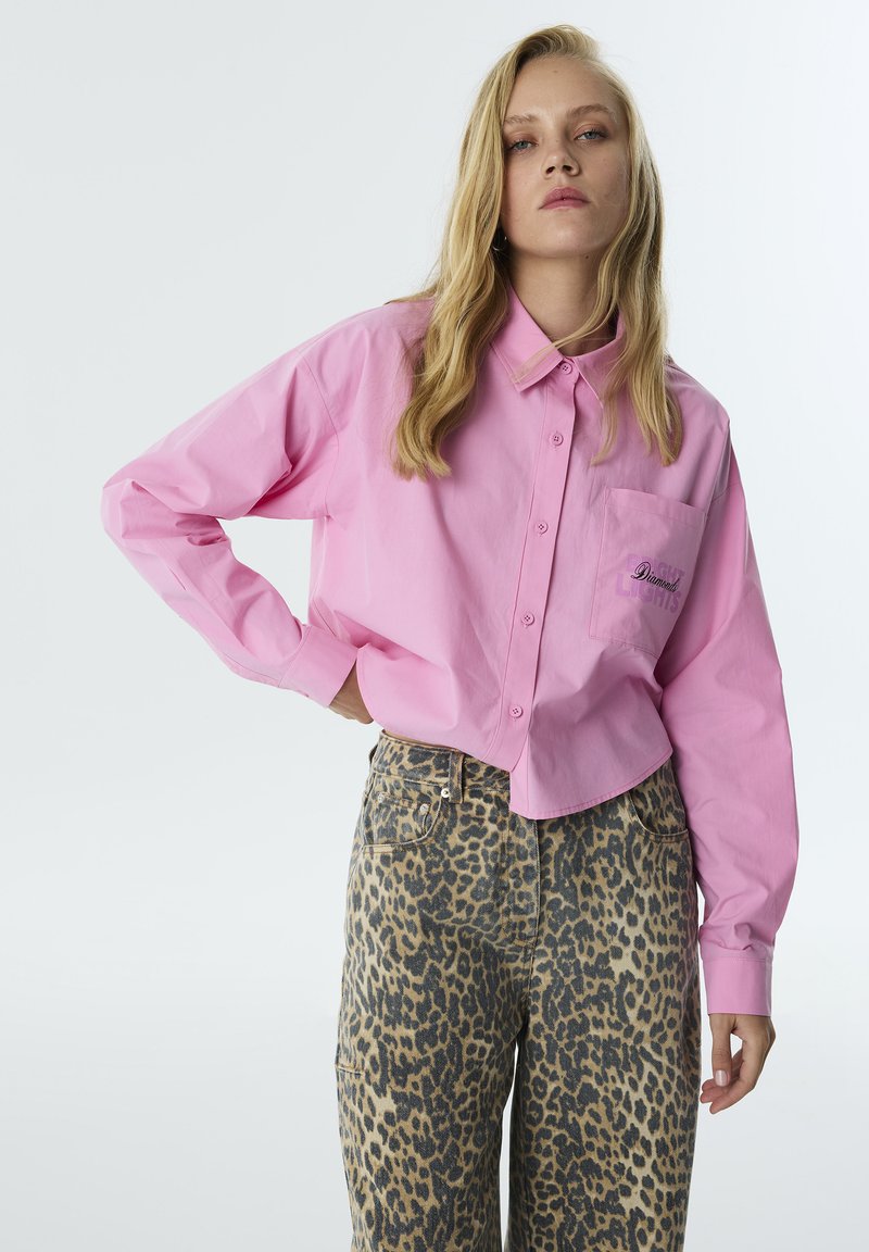 Roze overhemd met kraag en een zak met daarop de tekst "Diamond Lights", gecombineerd met hoog-was leeuwenhuid jeans. Beide hebben een ontspannen fit.