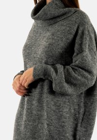 Un pull oversize doux et gris avec un col roulé et des manches longues, présentant un motif de tricot texturé et une coupe ample.