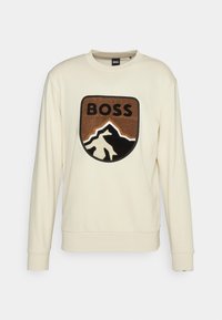 Beige sweatshirt with a crew neck, featuring a plush patch with mountains and the word "BOSS" in black and brown. Soft fabric, relaxed fit.