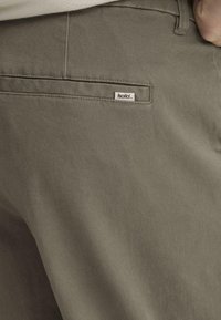 Pantalones verde oliva hechos de tela de algodón suave, con un bolsillo trasero que tiene una pequeña etiqueta blanca "isolid", diseño minimalista.