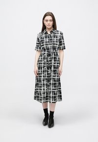 Rochie cămașă în carouri alb-negru, cu mâneci scurte, talie strânsă, lungime medie, cu guler și închidere cu nasturi.