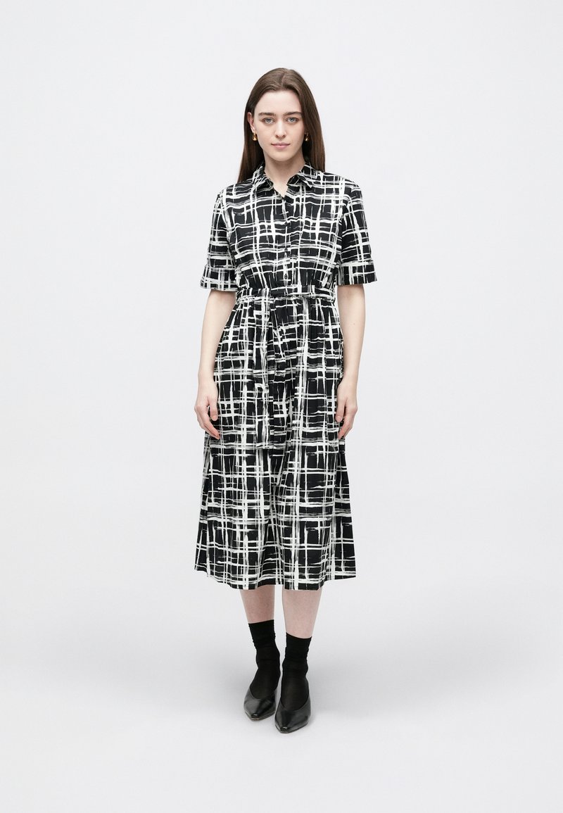 Rochie cămașă în carouri alb-negru, cu mâneci scurte, talie strânsă, lungime medie, cu guler și închidere cu nasturi.