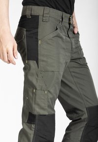 Pantalons cargo en vert olive foncé avec des accents noirs, présentant plusieurs poches, un tissu durable et des détails de couture jaunes.