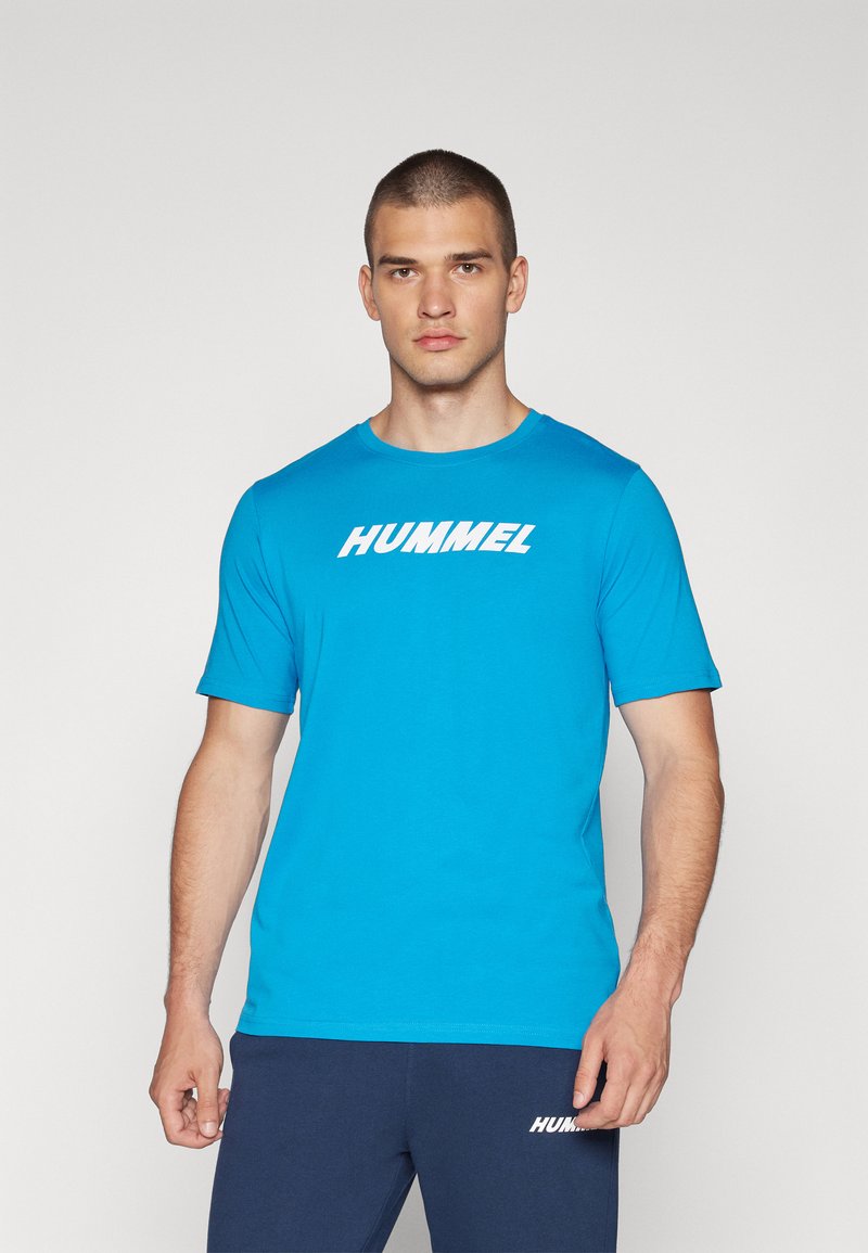 Camiseta de manga corta azul cielo hecha de una tela suave con cuello redondo. Presenta un destacado logo blanco de "HUMMEL" en el pecho.