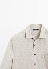 Helles graues Leinenhemd mit umgelegtem Kragen, dunklen Knöpfen, einer einzelnen Brusttasche und strukturiertem Stoff, der ein lässiges Design zeigt.