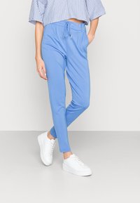 Lichtblauwe joggerbroek gemaakt van zachte stof met een trekkoord in de taille. Gecombineerd met witte sneakers, wat een relaxte pasvorm en taps toelopende pijpen toont.