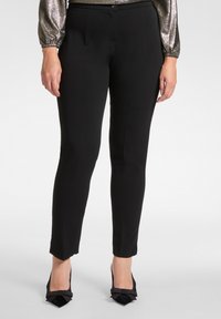 Schwarze, maßgeschneiderte Hose aus glattem Stoff, schlanker Schnitt und knöchellang, kombiniert mit schwarzen, spitzen High Heels mit einer Schleifenverzierung.