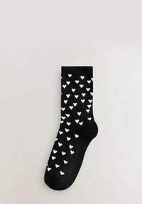 Schwarze Socke mit weißem Herzmuster, ausgestattet mit einem gerippten Bund, glatter Textur und mittellanger Länge.
