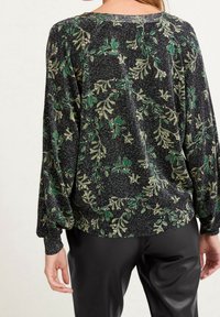 Maglione nero con filo metallico, caratterizzato da motivi di foglie verdi e beige. Spalle scese e vestibilità ampia con polsini a coste.