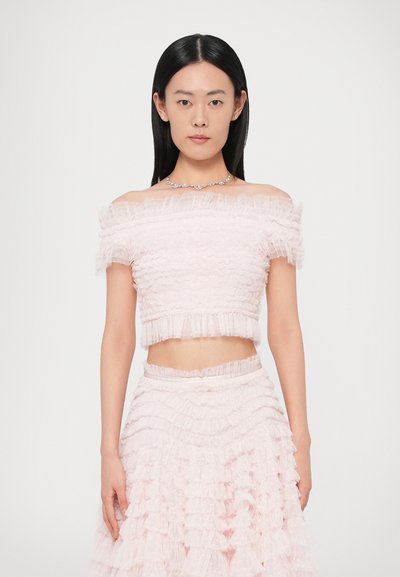 Ensemble rose deux pièces comprenant un haut court à volants, épaules dénudées, et une jupe à volants en plusieurs couches avec une taille cintrée. La texture semble douce et délicate.