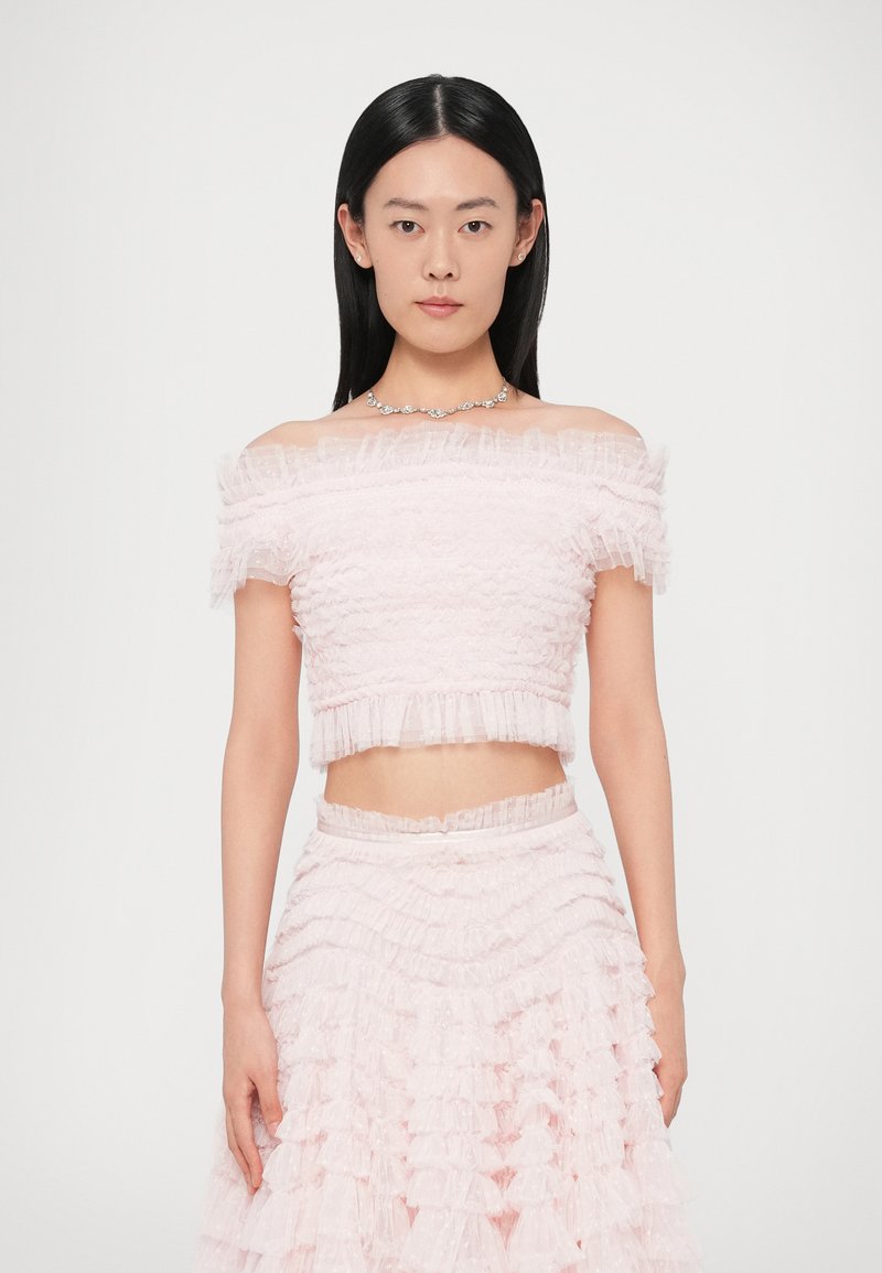 Lyserødt todelt sæt med en kort, flæset off-shoulder top og et lagdelt, flæset nederdel med en figursyet talje. Teksturen virker blød og delikat.