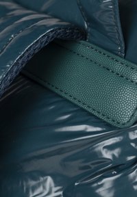 Material acolchado de color teal con un acabado brillante, que presenta un acento de cuero verde texturizado y bordes cosidos, mostrando un diseño de tela en capas.