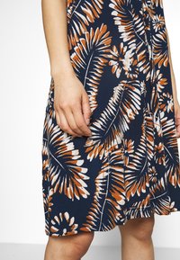 Robe marine avec un motif de feuilles tropicales en orange et blanc. Tissu doux, longueur genou, avec une silhouette évasée et une couture latérale.