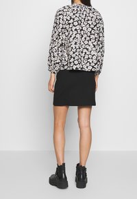 Blouse noire à fleurs avec manches bouffantes, associée à une mini-jupe noire et des bottes noires épaisses. Tissu lisse avec un motif floral délicat.