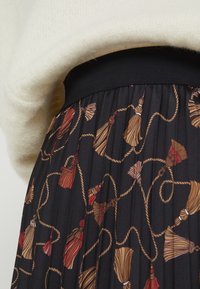 Svart plisserad kjol med ett mönster av rep och tofsar i röd och beige. Har en bred, elastisk svart midjeband.