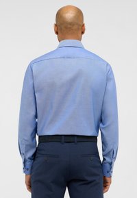 Hellblaues Langarmhemd mit strukturiertem Kragen, Knopfmanschetten und glatter Textur, kombiniert mit dunkelblauen Hosen mit Gesäßtaschen.