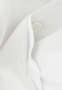 Primer plano de tela blanca con una textura suave, presentando un botón y bordes doblados, mostrando un diseño sencillo y material ligero.