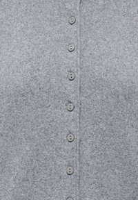 Gros plan sur un tissu tricoté gris avec une rangée verticale de sept petits boutons ronds gris.