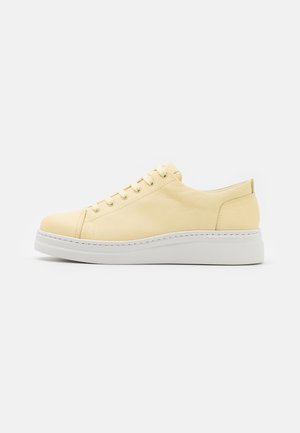 Niski żółty skórzany sneaker z białą grubą podeszwą i sznurowanym zapięciem, pokazany z boku na jasnym jednolitym tle.