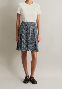 Krämfärgad t-shirt med kort ärm tillsammans med en svart kjol med ett ljusblått abstrakt mönster. Svarta vävda sandaler fullända outfiten.