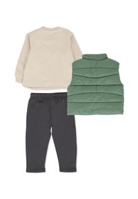 Felpa beige, gilet verde imbottito con texture trapuntata e pantaloni della tuta neri. Tutti gli articoli presentano una vestibilità rilassata e materiali morbidi.