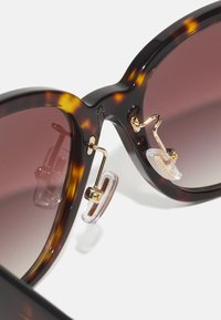 Tortoiseshell sunglasses with gradient brown lenses, gold metal accents, and clear nose pads. Features oversized, rounded frames.