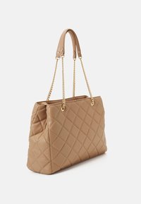 Beige kviltad läderhandväska med dubbla guld kedjor och läderhandtag, rektangulär form och rymlig öppen topp.