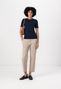 Tricou de marină cu mâneci scurte, cu dungi, asortat cu pantaloni bej albați, ajustați, și pantofi negri tip slip-on. Geantă de umăr simplă din piele maro.