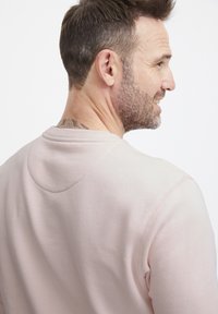 Felpa rosa chiaro con scollo tondo e texture morbida, con dettagli di cucitura. Il design include una sottile cucitura sulla spalla.