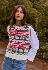 Knit holiday sweater vest with multicolored patterns, including "JOYEU NOEL" text. Features a ribbed hem and contrasts with a white long-sleeve shirt.