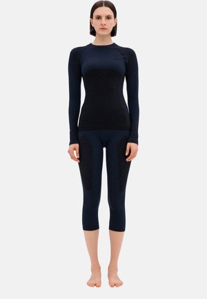 Abbigliamento sportivo aderente di colore blu scuro, con maniche lunghe e leggings fino al ginocchio con dettagli testurizzati sulle gambe.