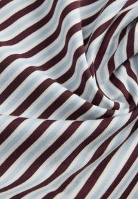 Pehme kangas horisontaalsete triipudega helesinisest ja tumedast burgundia värvist, mis näitab õrnu voltse ja tekstuuri detaile.