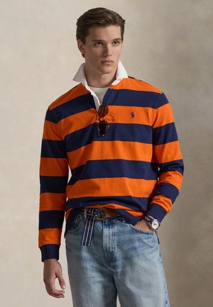 Koszulka rugby z długim rękawem z pomarańczowymi i granatowymi poziomymi paskami, kołnierzyk, luźny krój, zestawiona z wyblakłymi niebieskimi dżinsami i paskiem w paski.