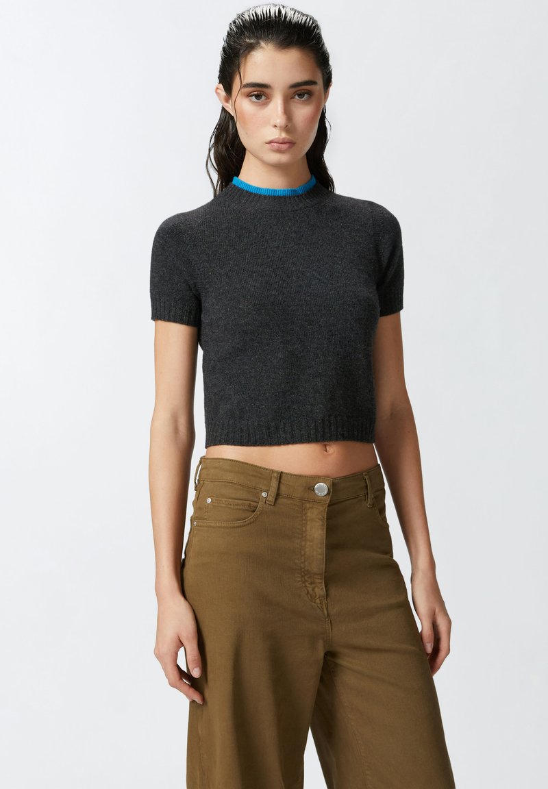 Sivi kratki pleteni top s rebrastim izrezom koji ima plavu akcentu. Uparen s high-waisted bež širokim hlačama.