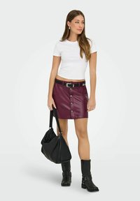 Přiléhavé bílé tričko je kombinováno s vínovým koženým mini sukněm s předními knoflíky a černým páskem. Celkový outfit doplňují černé kotníkové boty a kabelka.