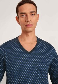 Marineblauwe V-hals shirt met een klein bloemenpatroon in lichtblauw, voorzien van een borstzak en een zachte, ademende stofstructuur.