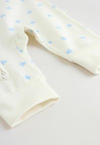 Krupni plan bijelih bebi hlačica s rebrastim uzorkom, svijetloplavim zvjezdicama i preklopljenim rubovima na bijeloj površini.