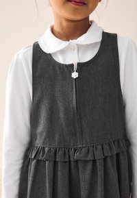 Gray denim dress with ruffled hem and a zip closure featuring a white flower pull tab, layered over a white collared shirt.