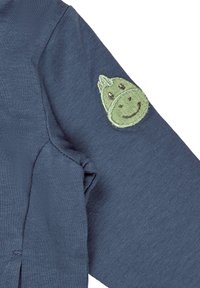 Marineblaues Langarmshirt mit einem grünen, gestickten Smiley-Gesicht auf dem linken Ärmel. Der Stoff hat eine gerippte Textur.