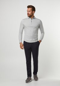 Polo grigio chiaro a maniche lunghe con colletto e tre bottoni, abbinato a pantaloni scuri e sneakers grigie. Texture liscia, design casual.