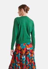 Cárdigan verde de punto con mangas largas y cintura ajustada, combinado con una falda de patrón colorido en tonos rojos, azules y verdes.