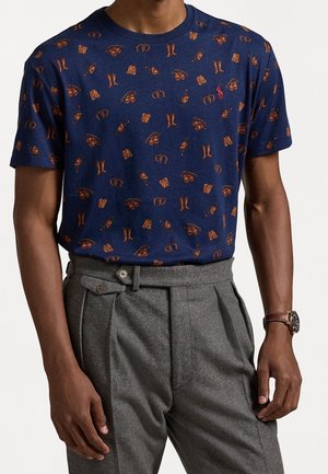 Granatowy bawełniany t-shirt z powtarzającym się wzorem brązowego sprzętu wędkarskiego, w tym rękawic, butów i dzwonka. Okrągły dekolt i krótkie rękawy.