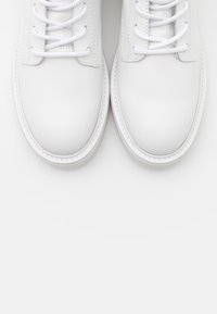 Weiße Leder-Sneaker mit einer glatten Oberfläche, runden Zehen, sechs Ösen für Schnürsenkel und genähten Details entlang der Gummisohle.