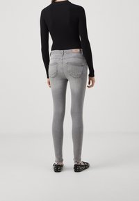 Jeans grises ajustados con efecto desgastado, cinco bolsillos y costuras contrastantes. Combinados con una blusa negra de canalé y bailarinas negras con tachuelas.