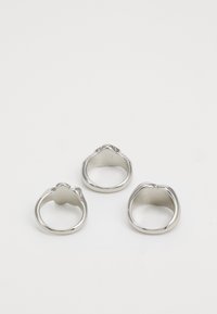 Tres anillos de plata con superficies lisas y brillantes. Uno tiene un diseño único en la parte superior, que se asemeja a un emblema. Todos los anillos son redondeados y metálicos.