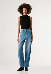 Top negro sin mangas con detalles de botones en los hombros, combinado con vaqueros de pierna ancha de talle alto en azul claro y botines negros.