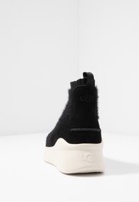 Černá kotníková teniska s chlupatou texturou, vyrobená z semiše a syntetických materiálů, s bílou podrážkou a táhlem pro snadné obouvání.