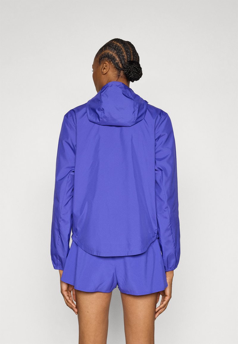 Veste légère violette avec capuche, dotée d'une texture lisse, de manches longues et d'un ourlet légèrement arrondi. Associée à un short assorti.