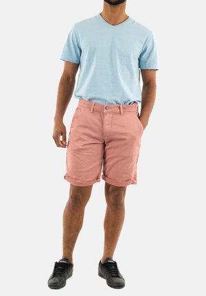 Camiseta de cuello en v de color azul claro con mangas cortas, combinada con pantalones cortos de algodón rosa enrollados. Zapatillas negras completan el conjunto.